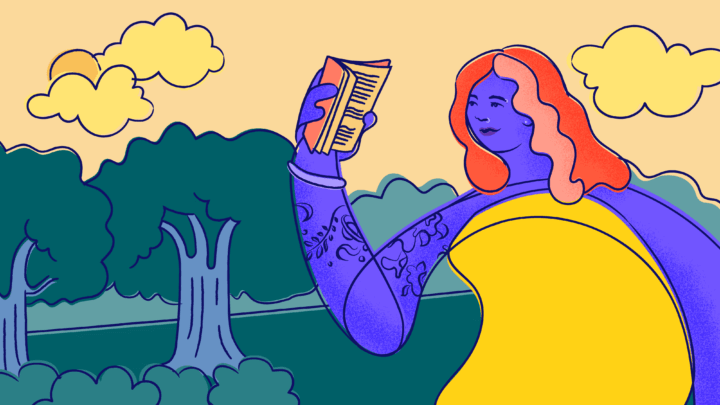 A female-presenting young person in a yellow dress reads a book as they walk next to some trees on a cloudy day.