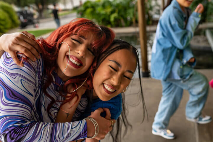 Two LGBTQ+ young people hug and laugh joyously.