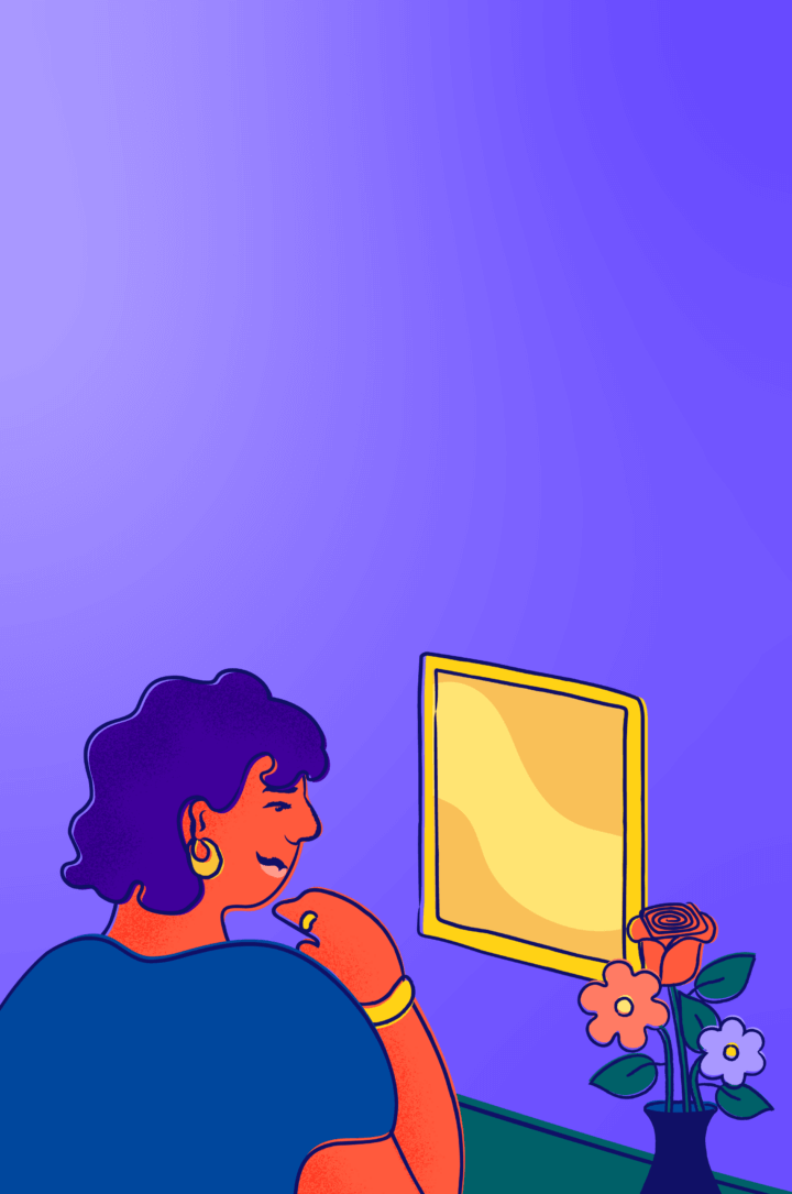 A young person at a desk with flowers smiles and looks in the mirror.