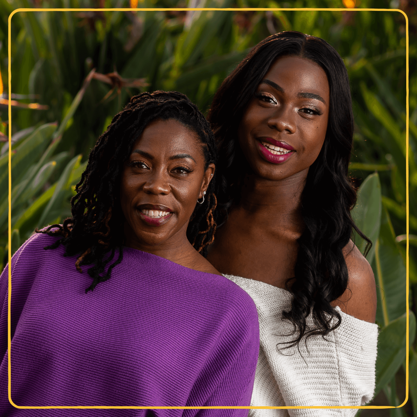 An LGBTQ+ young person smiles with her mom in front of foliage.